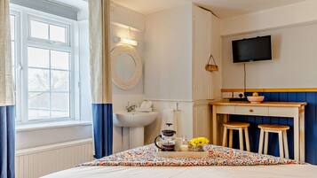 A bedroom with a bed, a bedside table with a tray of breakfast items, a sink, and a TV mounted on the wall.