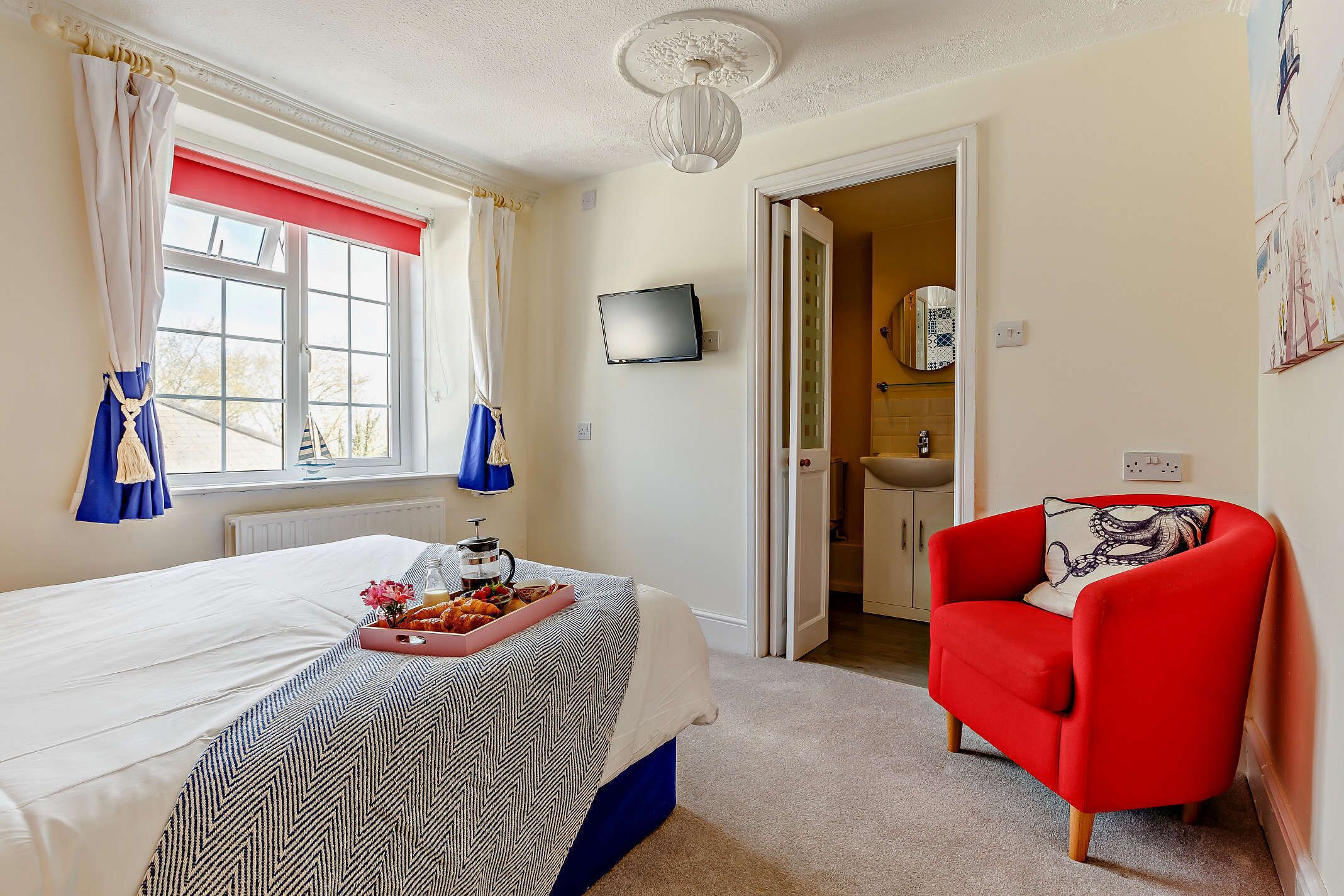 A hotel room with a bed, a red armchair, a television, and a bathroom visible through an open door.
