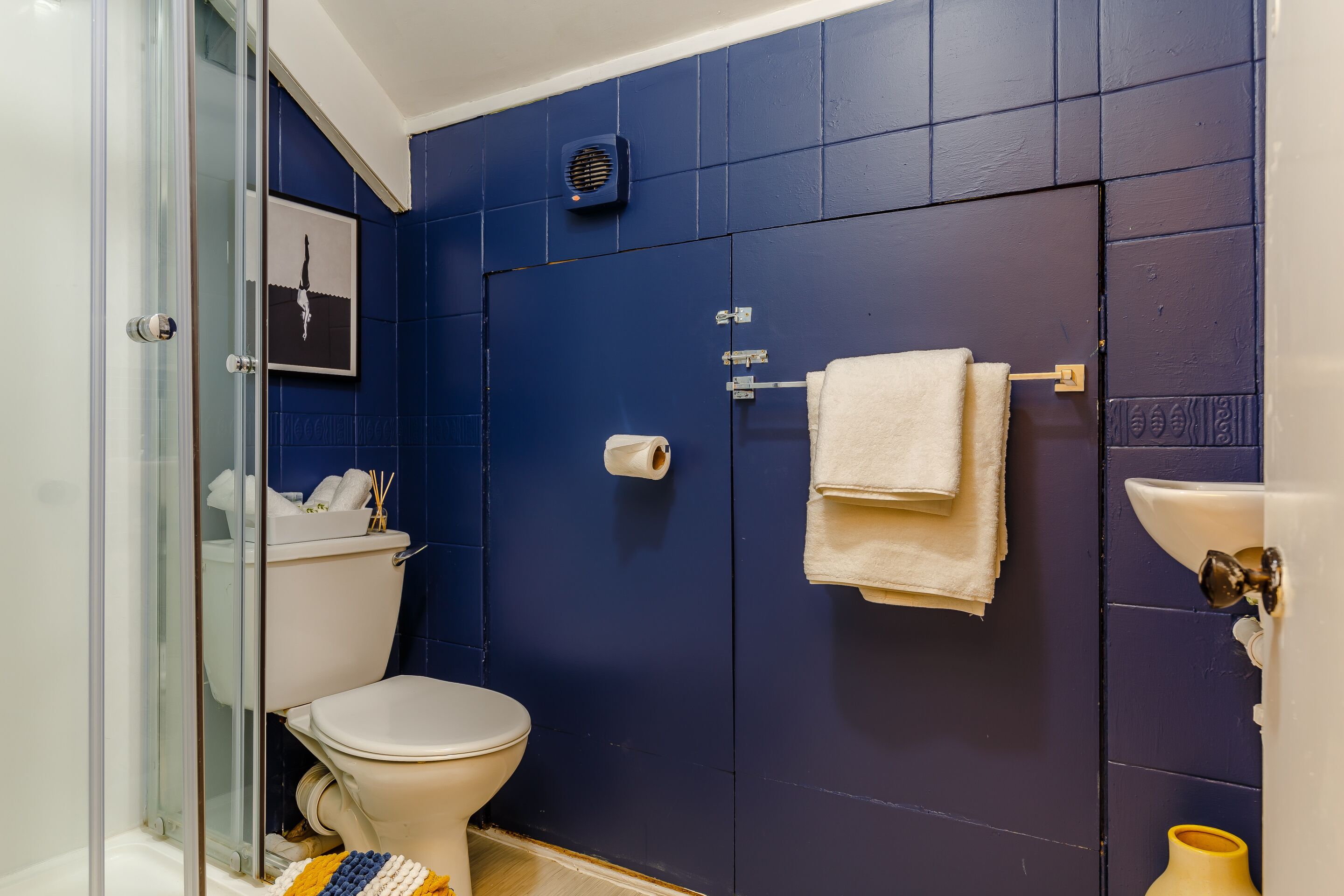 Un baño con inodoro, cabina de ducha de vidrio, lavamanos y perchero para toallas.