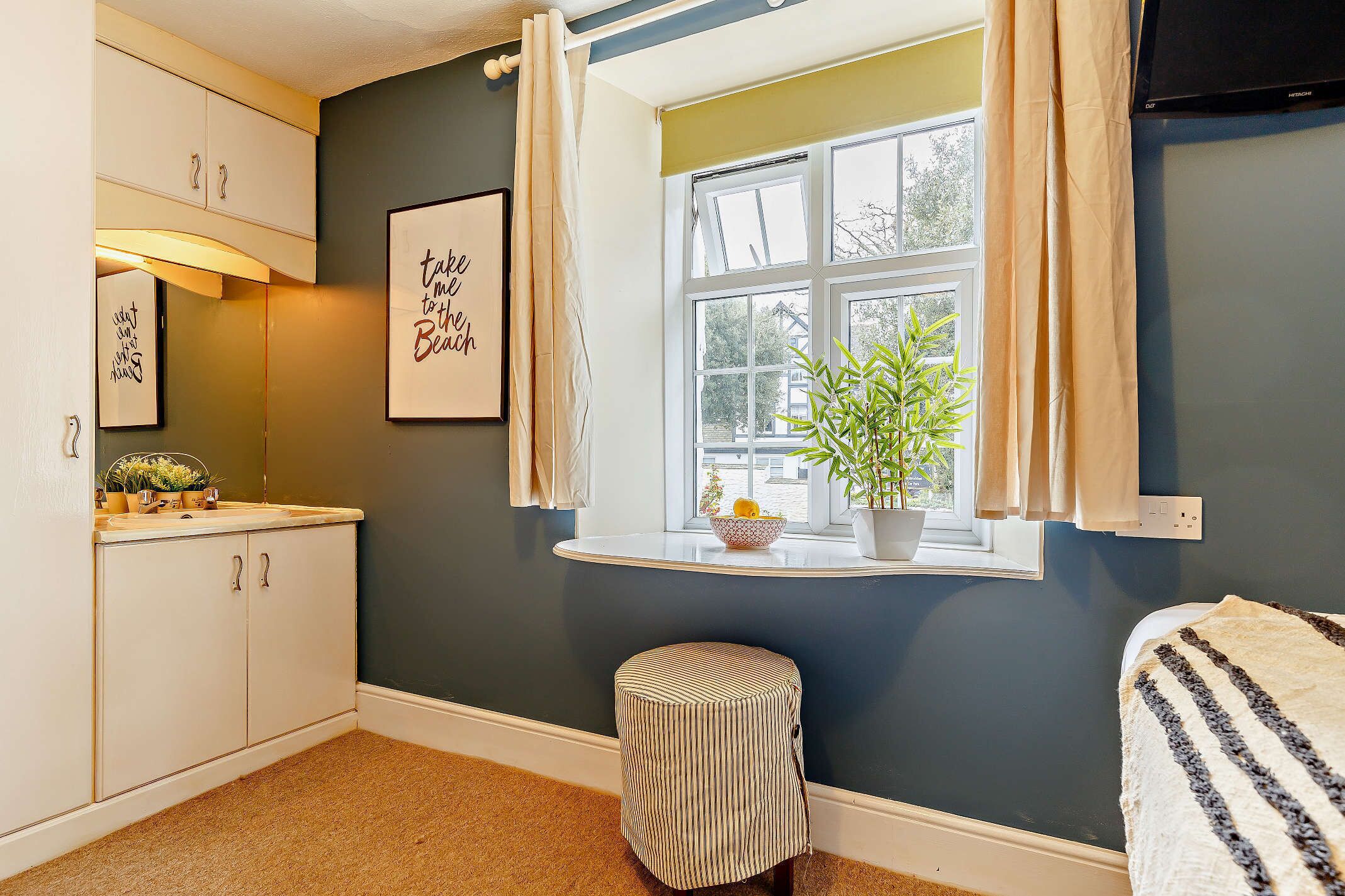 A bedroom with a window, a bedside table, a small stool, and a bed.