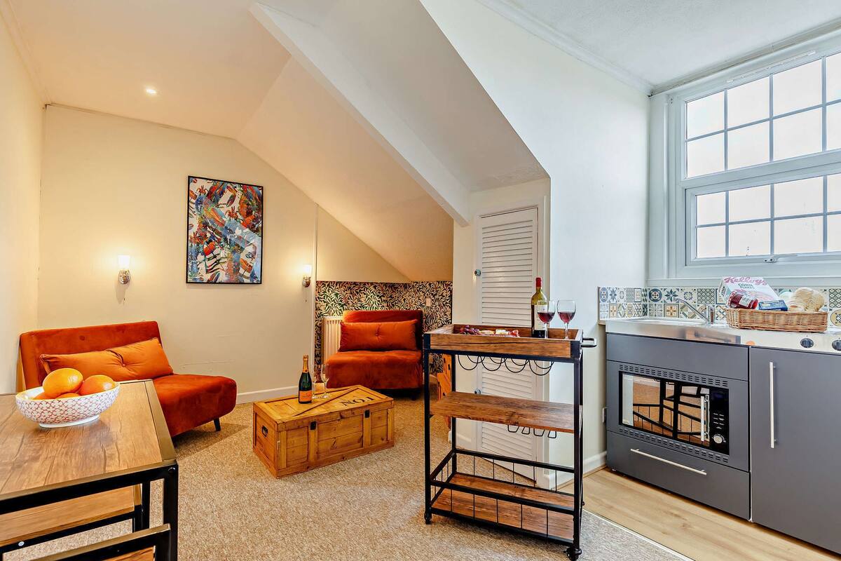 Un espacio habitable compacto con un entrepiso de dormitorio, una kitchenette, un comedor y una sala de estar con un sofá y una mesa de centro.