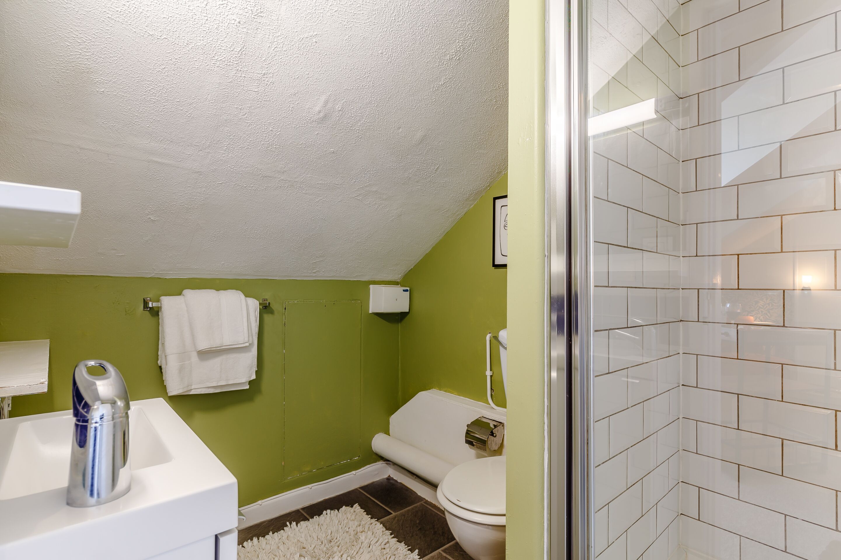 A bathroom with a green wall, white fixtures, and a shower area.