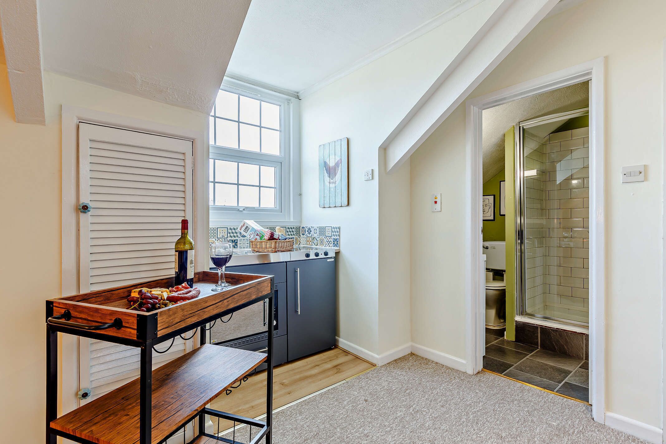 A compact kitchen with a wooden table, a window, and a shower area visible through an open door.