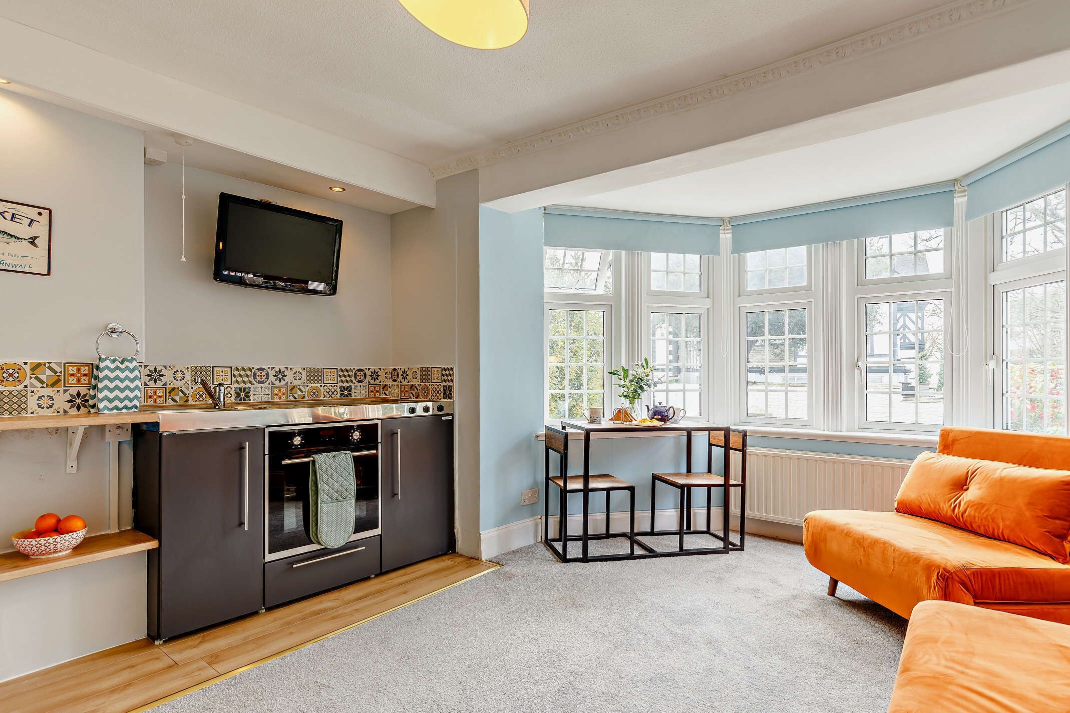 Eine moderne Küche mit Einbauofen und Flachbildfernseher. Ein Essbereich mit Tisch und Stühlen lädt zum Verweilen ein, und ein großes Fenster sorgt für natürliches Licht.
