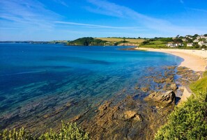 A coastal landscape with clear waters, rocky shoreline, and houses in the background. - 1605 by the sea (Falmouth)