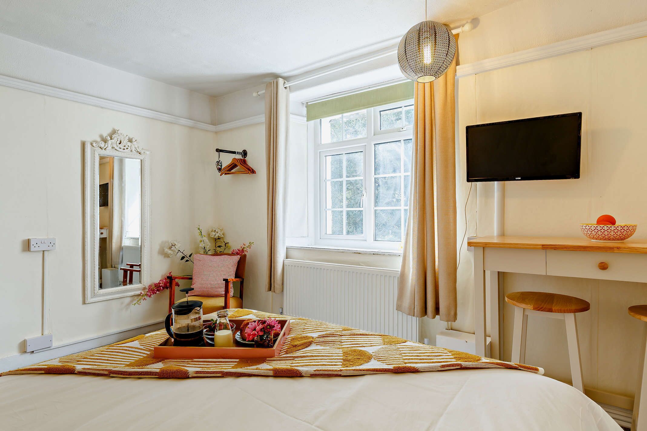 A bedroom with a bed, a dresser, a television, a window with curtains, and a mirror.