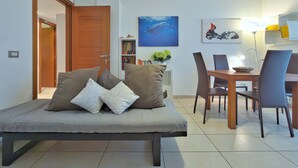 Una sala de estar moderna con un sofá, una mesa de comedor con sillas, una estantería y un cuadro en la pared.