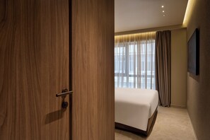 Ein Hotelzimmer mit Holzschrank, Bett, einem Vorhangfenster und einem Wand-Fernseher.