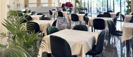 A spacious dining area with tables and chairs, a chandelier, and large windows.