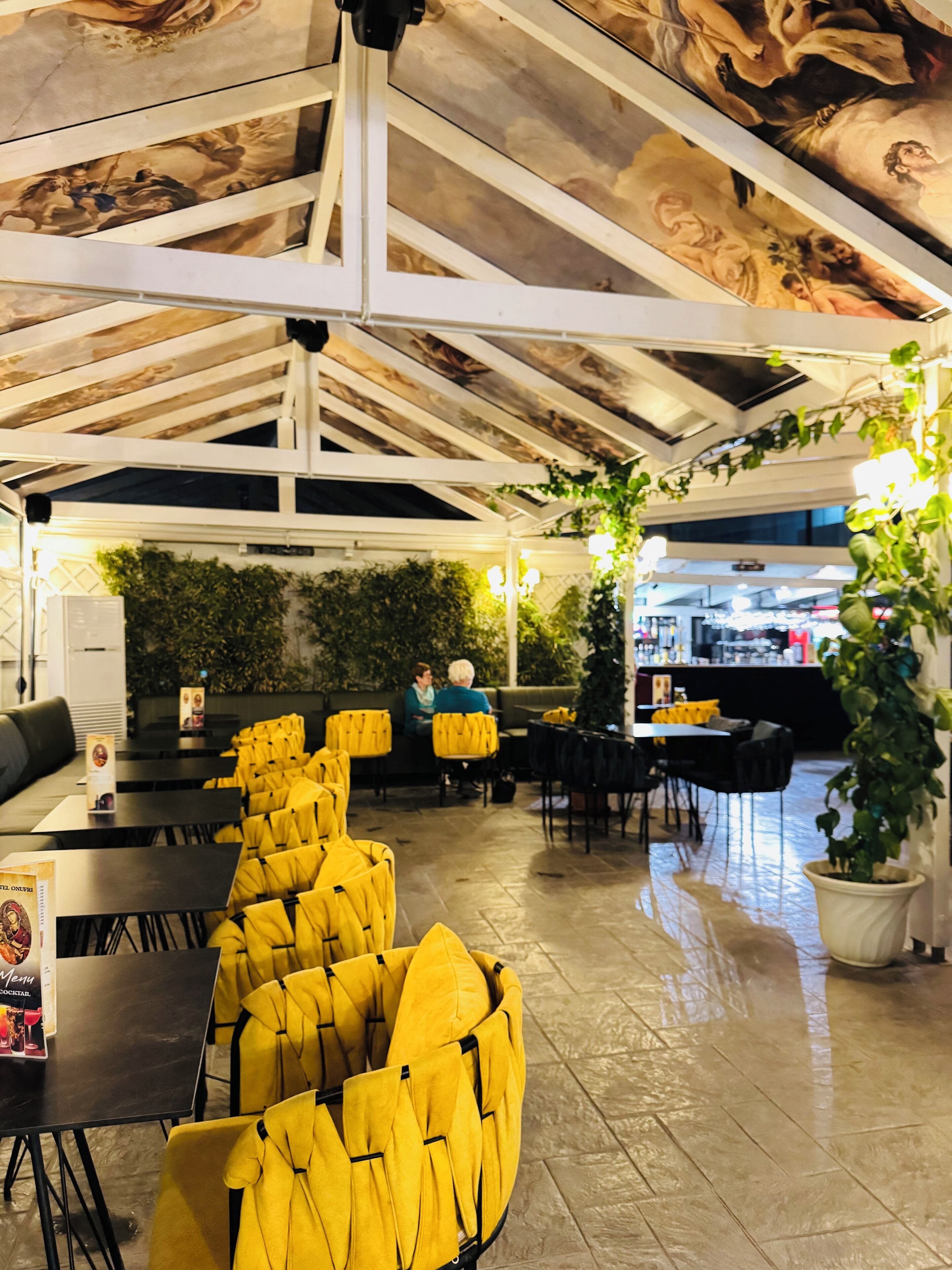 Un restaurante con techos altos, una zona de bar y diferentes disposiciones de mesas.