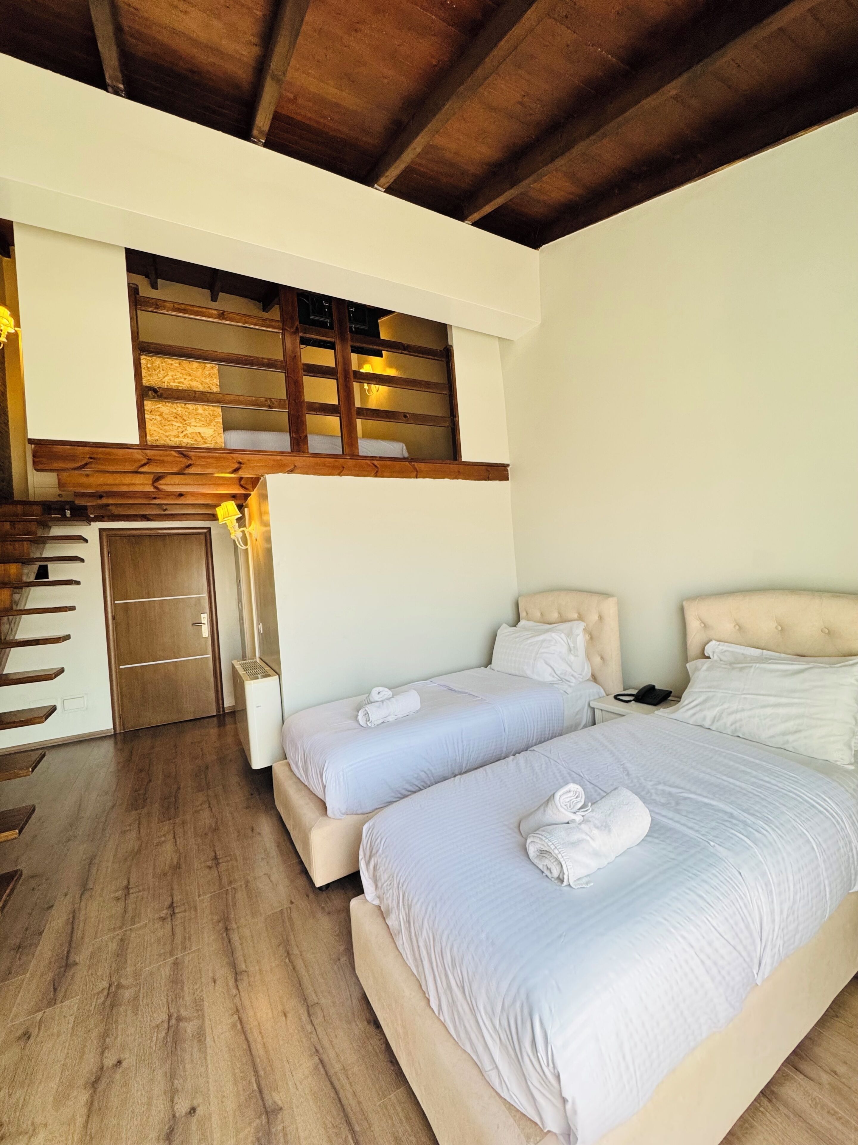 A hotel room with two beds, a wooden staircase, and a small balcony.