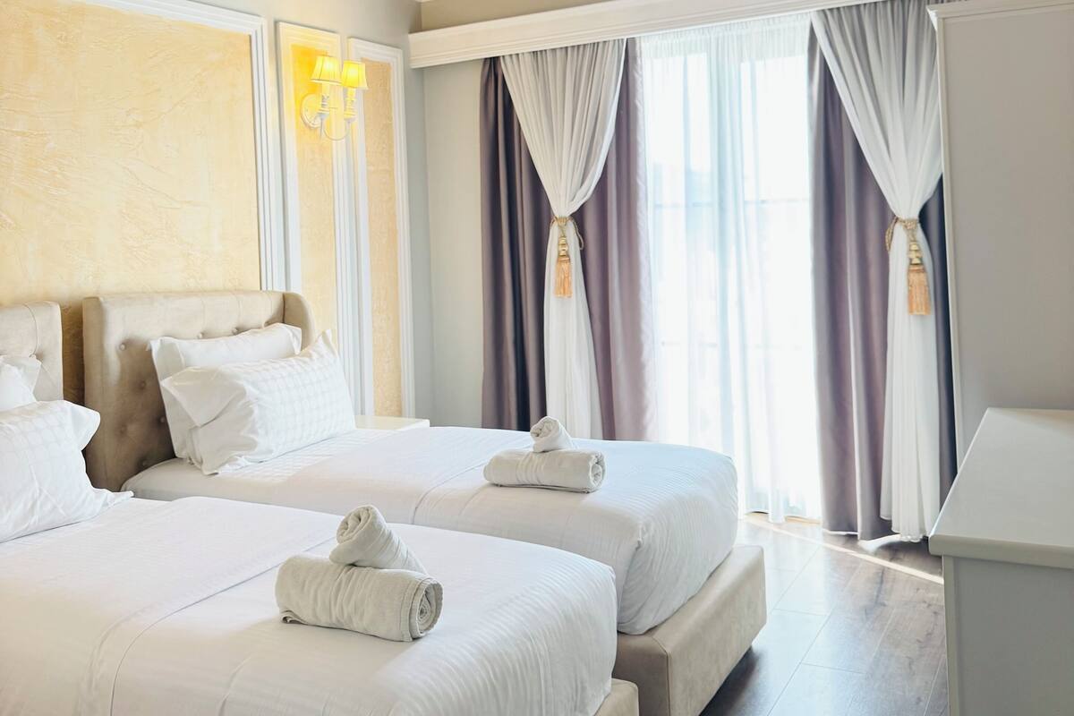 A hotel room with two beds, a desk, and a large window with curtains.