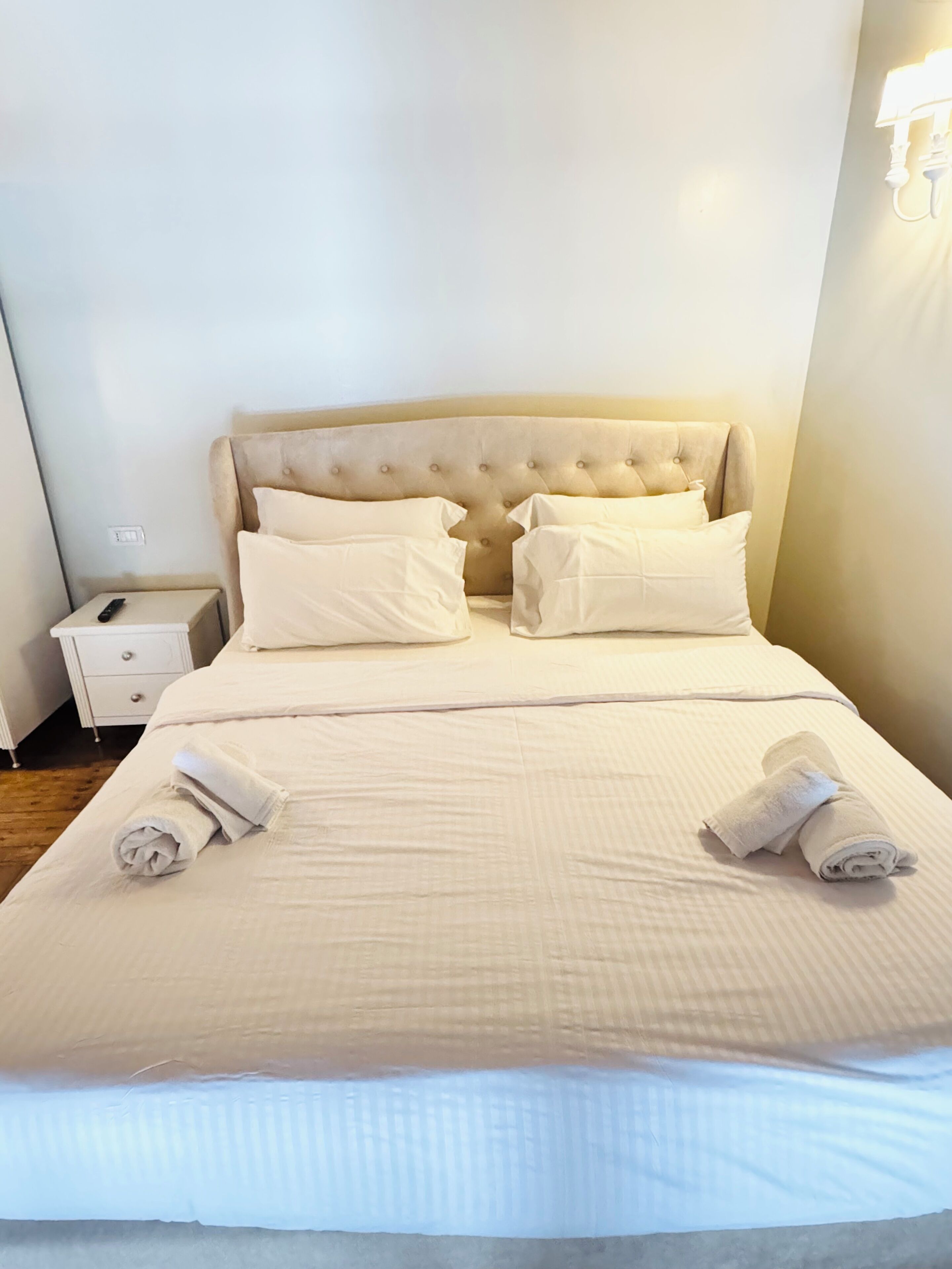 A neatly made bed with a tufted headboard, two pillows, and two rolled towels on the bed.