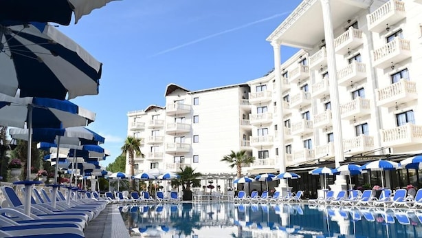 A poolside area with sun loungers and umbrellas, a clear sky, and a multi-story hotel building in the background. - Hotel Onufri (Golem)