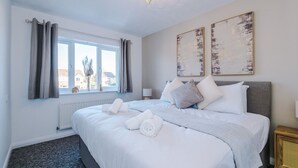 A hotel room with a large bed, grey curtains, a window with a view, and two abstract paintings on the wall.