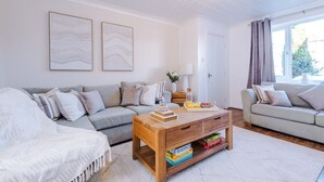 A modern living room with a sofa set, a coffee table with books and a tray, and a window with curtains.