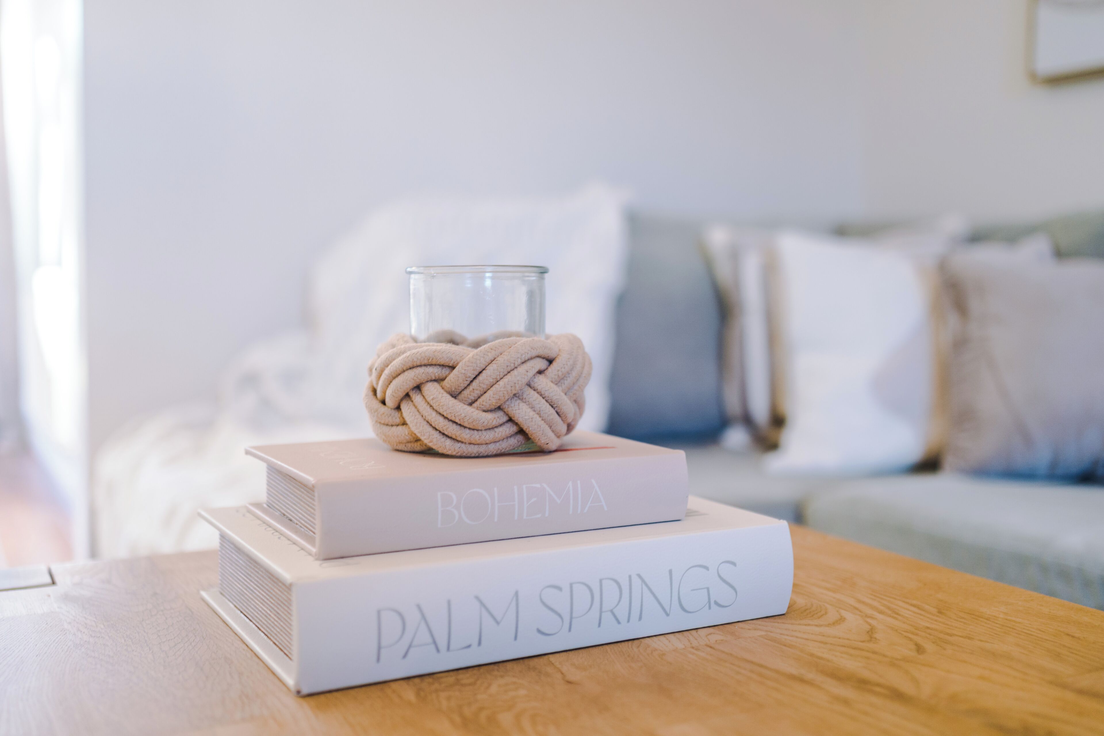 Een houten tafel met twee boeken getiteld 'BOHEMIA' en 'PALM SPRINGS' en een glazen pot met een knopen touw.