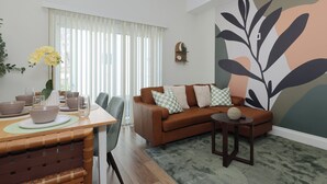 A living room with a brown sofa, a dining table with chairs, and a large wall mural.