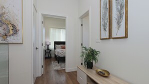 A hallway with a wooden floor, a bench with a plant, and a bed in the background.