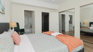 A modern hotel room with a large bed, a desk, and a chair. There are doors leading to other rooms and a bathroom.