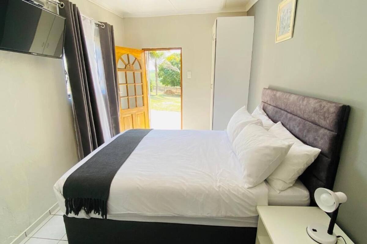 Un dormitorio con cama, lámpara de noche, televisor montado en la pared y puerta que da a un espacio exterior.