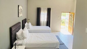 A hotel room with two beds, a window with curtains, a door leading outside, and a ceiling light. - Phola la bed and Breakfast (eMthonjaneni)