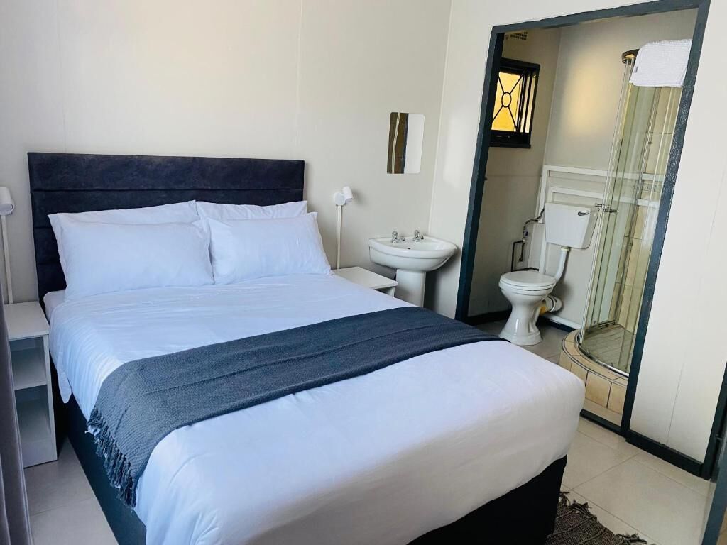 Una habitación de hotel con una cama, una mesita de noche, un lavabo blanco y un inodoro.