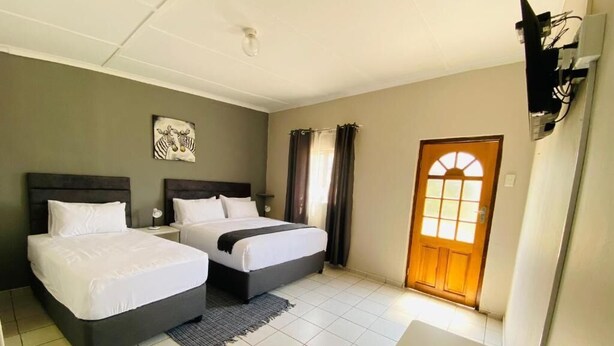 A hotel room with two beds, a wooden door, and a small table. - Phola la bed and Breakfast (eMthonjaneni)
