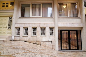 Un edificio de dos pisos con fachada de piedra, ventanas amplias con rejas de metal y una puerta de entrada negra.