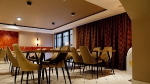 A dining area with a long table and multiple chairs, a patterned wall, and a large window. - Hortus Hotel Tirana (Tirana)
