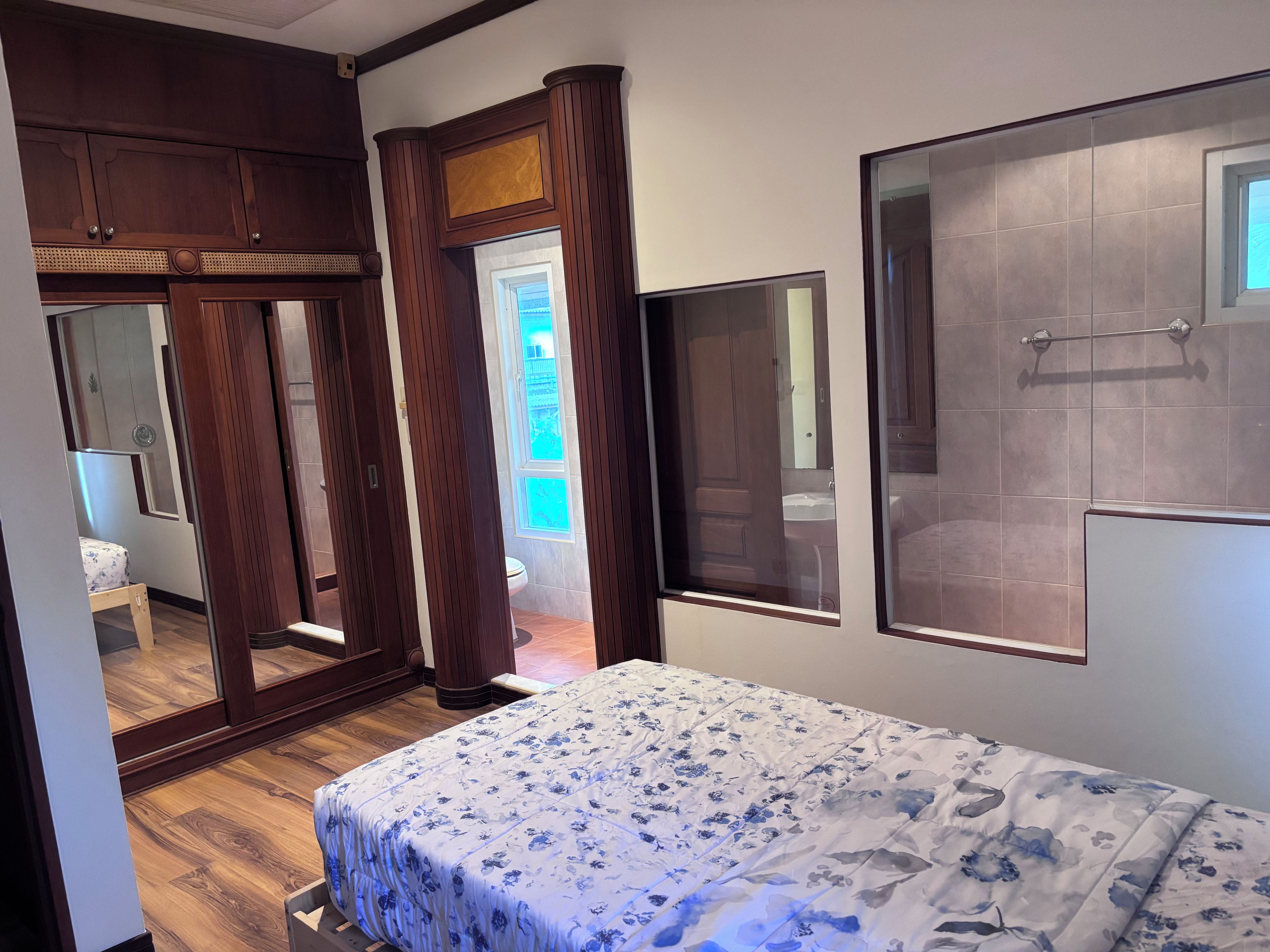 Une chambre à coucher avec un lit, une armoire en bois et une salle de bain visible à travers une porte.
