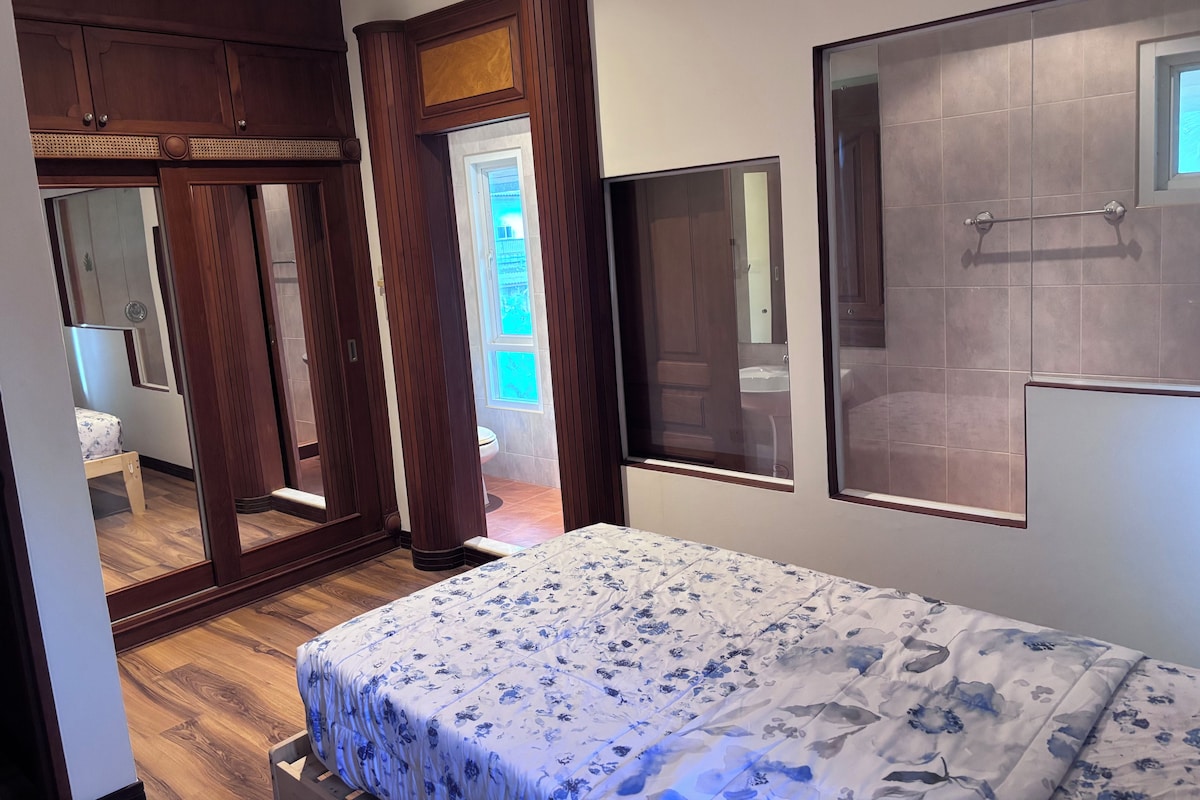 A bedroom with a bed, wooden wardrobe, and a bathroom visible through a door.