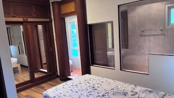 Une chambre à coucher avec un lit, une armoire en bois et une salle de bain visible à travers une porte.