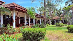 Un complejo turístico con varias construcciones tipo bungalow, cada una con un porche rodeado de exuberante vegetación y palmeras.