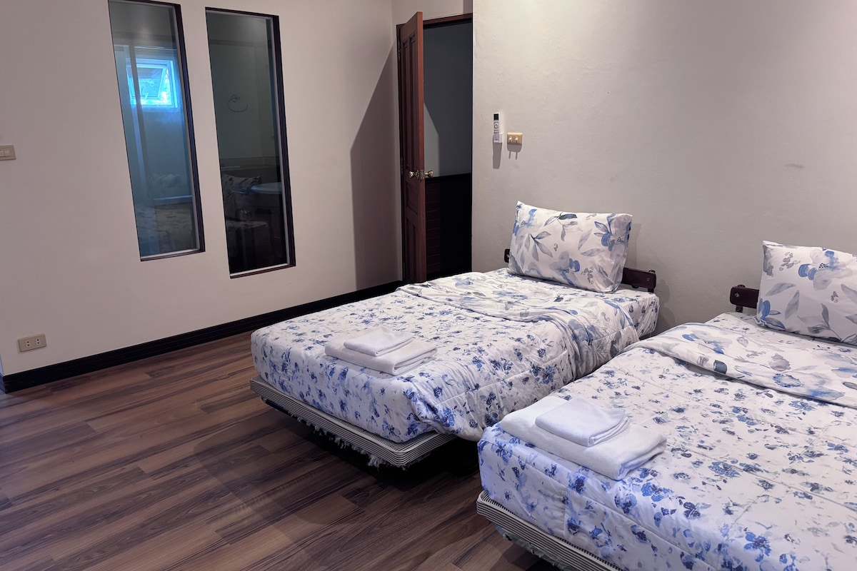 A hotel room with two beds, a wooden floor, a window, and a door.