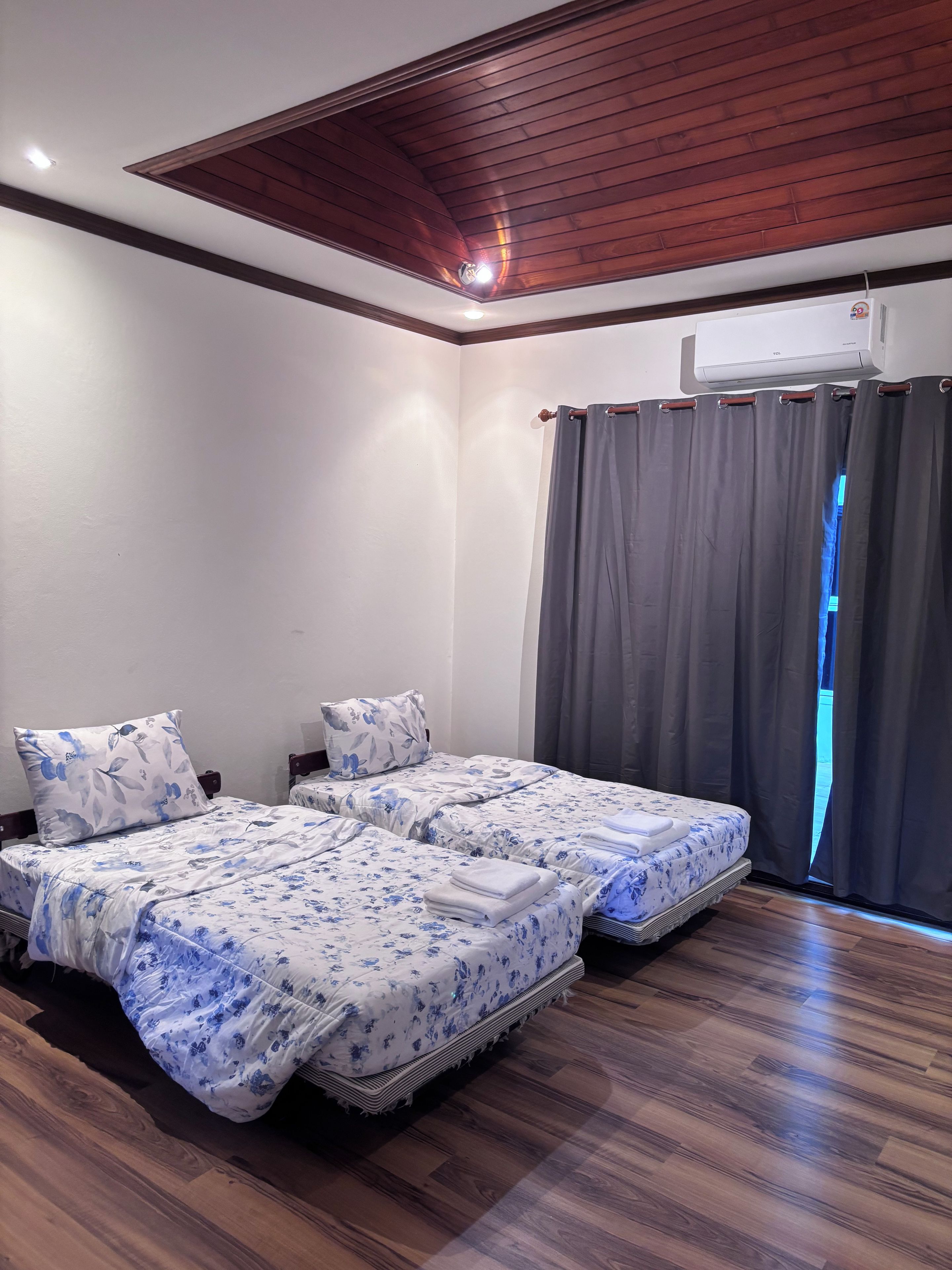 Una habitación con dos camas, ventilador de techo, aire acondicionado y una ventana con cortinas.