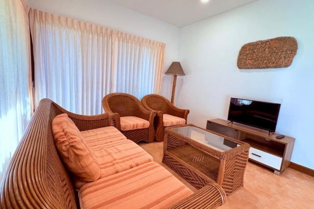 A living room with a sofa, two armchairs, a coffee table, a TV, and a lamp.