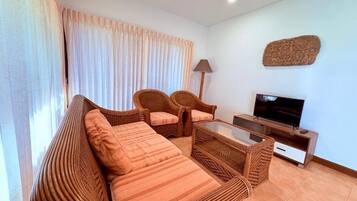 A living room with a sofa, two armchairs, a coffee table, a TV, and a lamp.