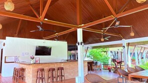 Un espacio al aire libre techado con un bar, asientos y ventiladores de techo.