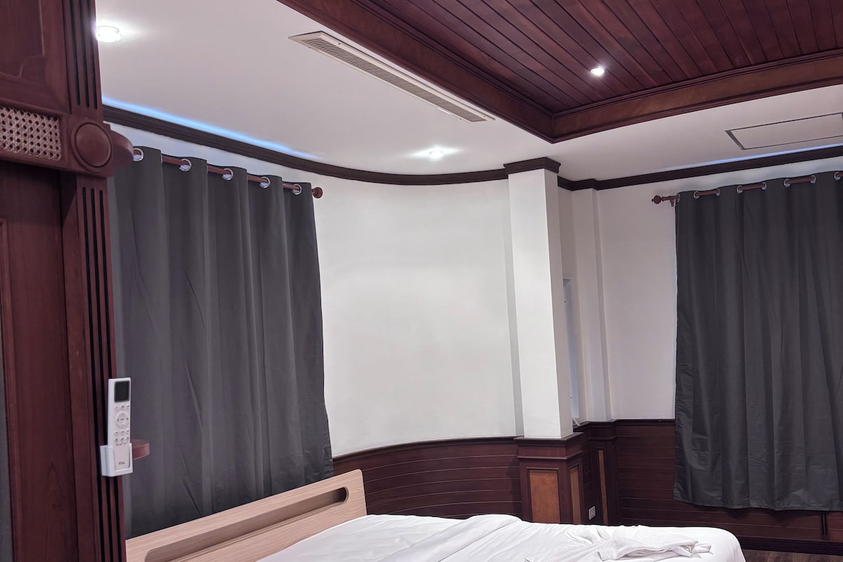 A bedroom with a wooden bed, a ceiling vent, and dark curtains.