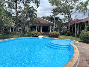 A swimming pool surrounded by lush greenery and a covered outdoor area with a tiled roof. - Kamala Garden Bungalows (Kamala)