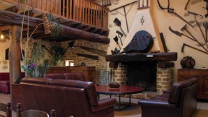 A rustic interior with leather sofas, a stone fireplace, and various tools on the wall.