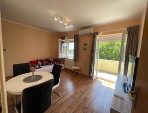Ein Zimmer mit Esstisch, Stühlen, einer Couch, einem kleinen Tisch und einem Fenster mit Vorhängen.