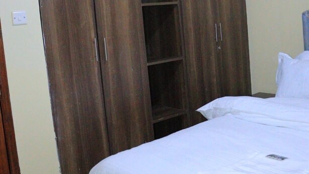Ein Schlafzimmer mit großem Kleiderschrank, einem Bett mit weißer Bettwäsche und einem Fliesenboden.