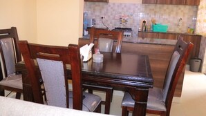 Ein Essbereich mit Holztisch und -stühlen, im Hintergrund eine Küche mit gefliestem Spritzschutz und ein Mülleimer in der Nähe des Spülbeckens.