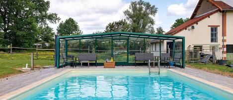Una piscina con cerramiento de vidrio, sillones de descanso y un muelle de madera.
