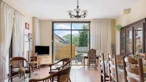 Comedor con sillas de madera, una mesa de vidrio, un televisor y vistas al exterior a través de un gran ventanal corredero.