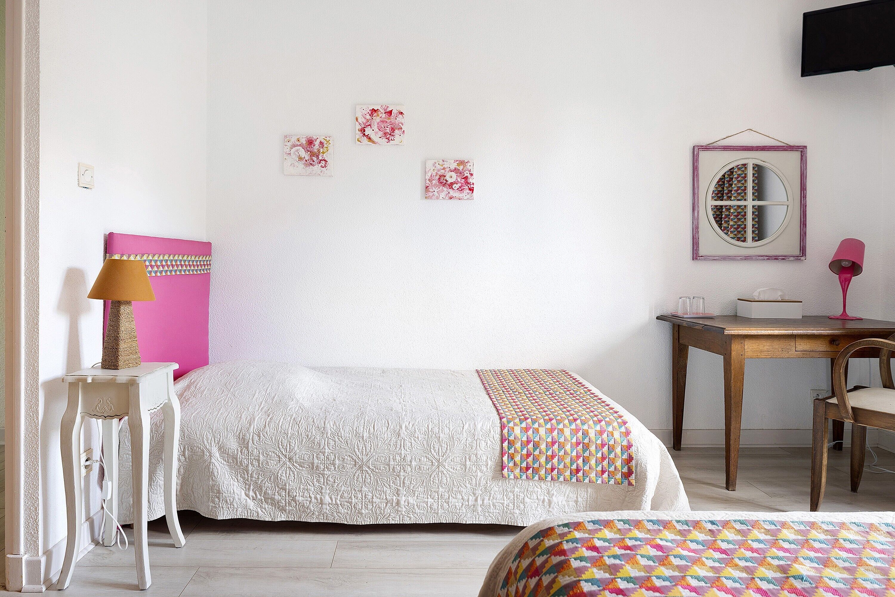 A bedroom with a bed, bedside table, lamp, and a desk with a chair.