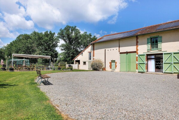 A building with a gravel driveway, green shutters, and a covered area with benches.