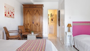 A hotel room with a bed, a chair, a desk, a wardrobe, and a bathroom visible through an open door.